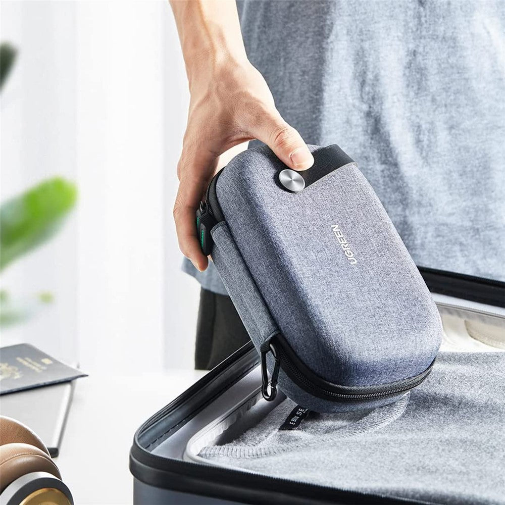 A person lowering the organiser into an open suitcase beside headphones and a laptop