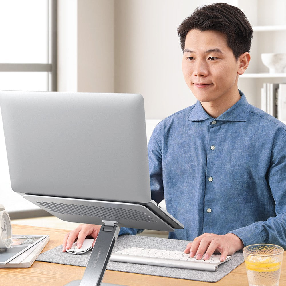 A man working at a desk with his laptop raised to eye level on the stand and a separate keyboard below