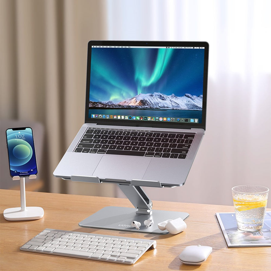 The stand on a wooden desk holding an open MacBook, with a phone, keyboard and mouse alongside