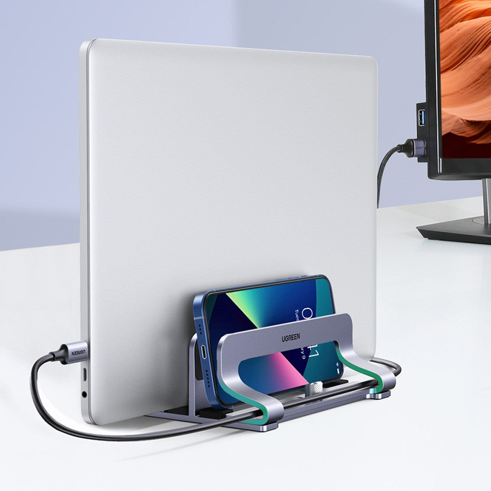 A laptop and a phone both docked in the stand in front of a monitor