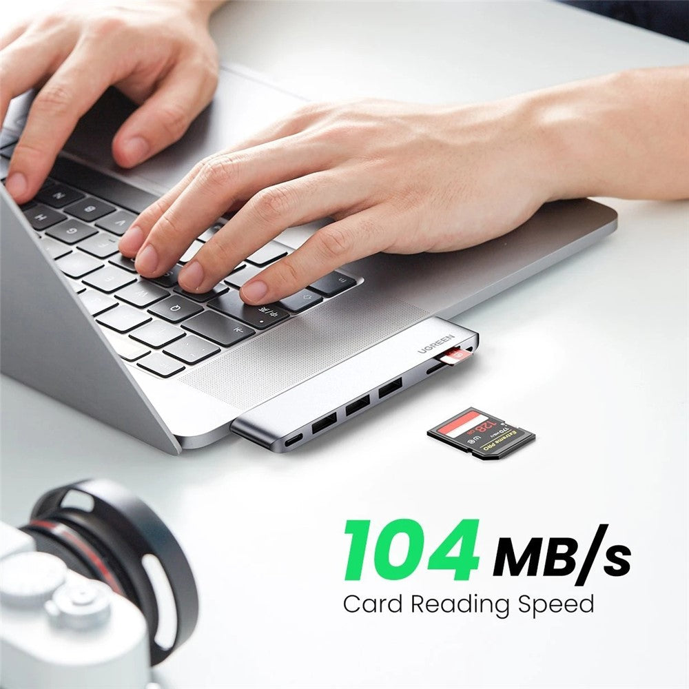 Hands typing on a MacBook with the hub fitted flush to the side and an SD card inserted, captioned 104MB per second card reading speed