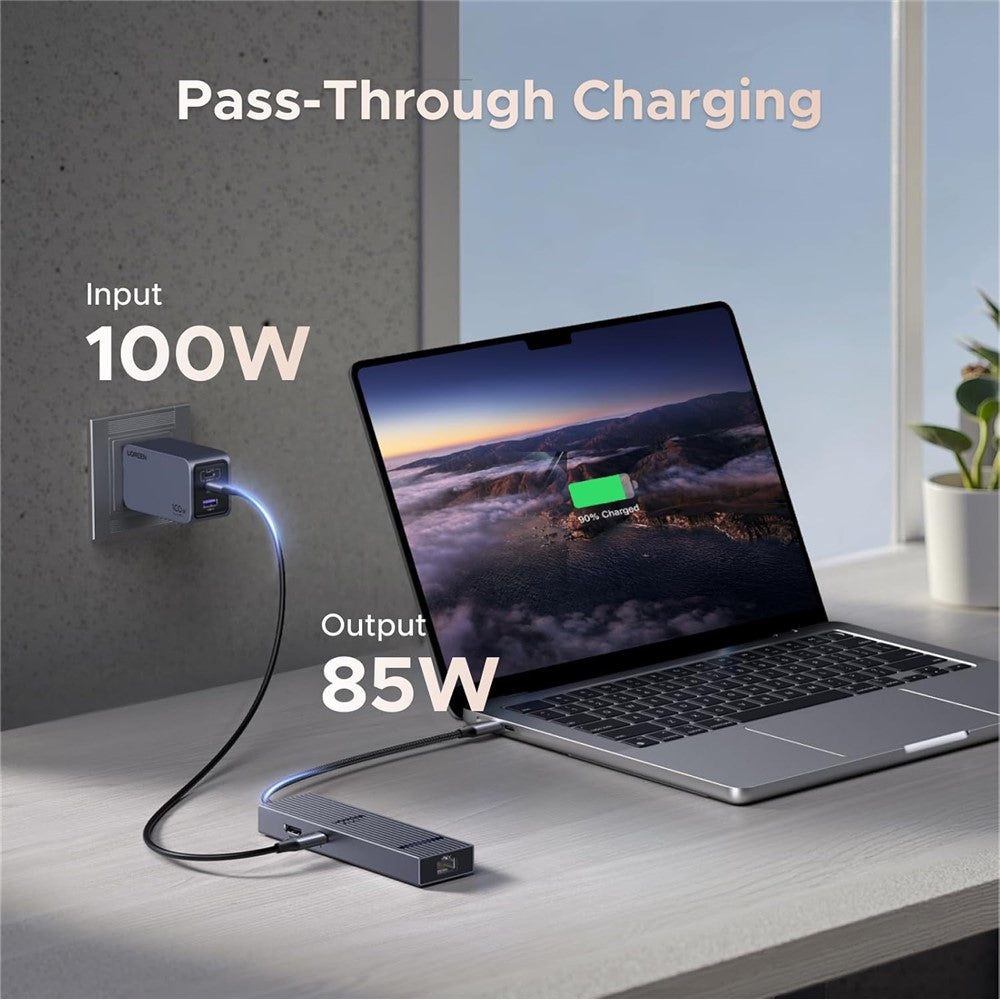 The hub connected between a wall charger and a MacBook on a desk, labelled 100W input and 85W output