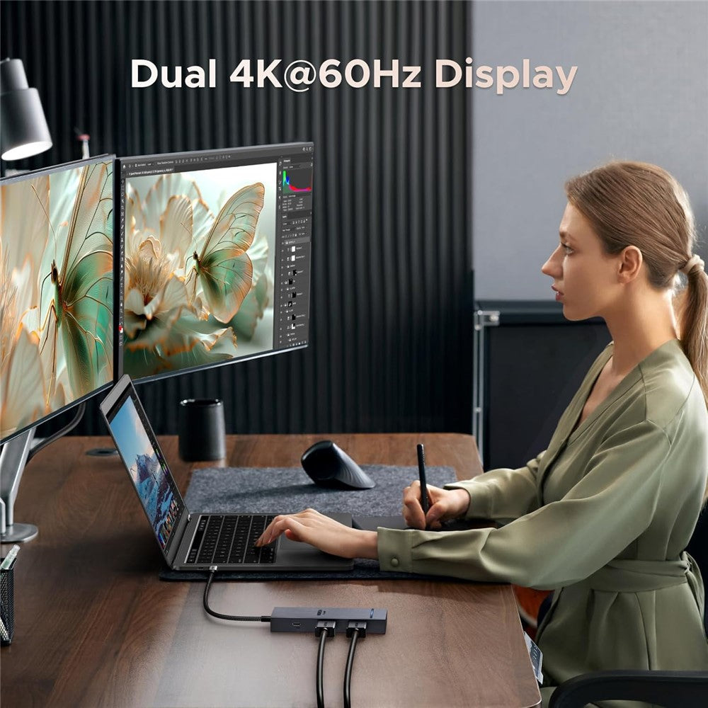 A woman working at a two-monitor desk setup with a drawing tablet, everything running through the dock