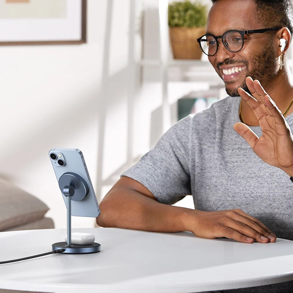 A man on a video call at a desk with his phone held upright in the charging stand